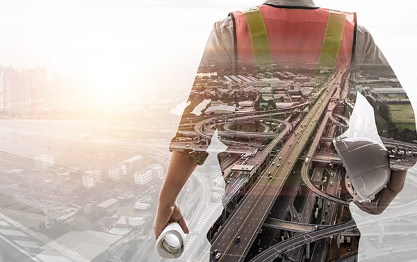 worker standing on the right holding a hard hat and blueprints